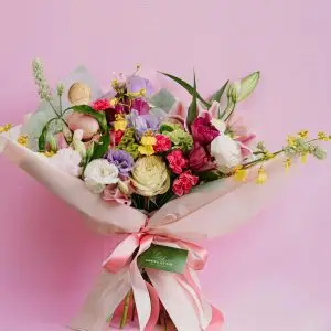 Charming mixed flower bouquet featuring roses and carnations against a pink backdrop.