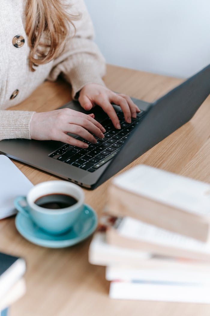 creative-01 Crop anonymous female freelancer surfing netbook while sitting at wooden table with cup of hot coffee and books in room